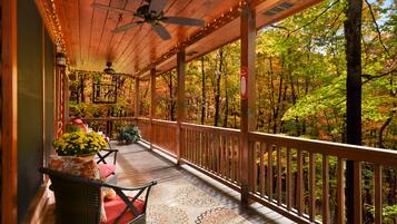 A covered porch with wooden railings, a ceiling fan, and string lights.