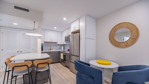 A modern kitchen with white cabinets, a central island with chairs, a microwave, and a refrigerator. - 1 Block to Beach, heart of Old Naples, newly renovated, perfect location (Naples)