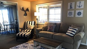 Ein Wohnzimmer mit einem gestreiften Sessel, einer Couch mit nautisch gestalteten Kissen und einem Couchtisch.