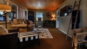 Ein gemütliches Wohnzimmer mit Holzbalkendecke, einer Couch, einem Couchtisch und einem Essbereich mit kleinem Tisch und Stühlen.
