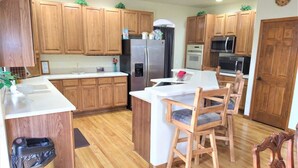 A kitchen with wooden cabinets, a stainless steel refrigerator, a microwave, and a dining area with wooden chairs.