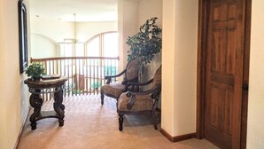 A hallway with a wooden door, a chair, a small table with a plant, and a staircase in the background.