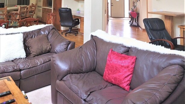 A spacious living area with a high ceiling, a wooden staircase, and a kitchen in the background.