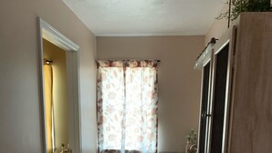A narrow hallway with a wooden floor, a patterned rug, a door leading to another room, and a window with floral curtains. - 2nd floor Downtown Apartment  (Gettysburg)