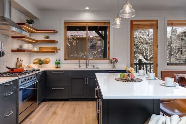 A modern kitchen with dark cabinetry, a central island, and wooden shelves.