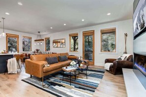 A modern living room with a sofa, coffee table, and fireplace. There are large windows and a kitchen area visible. - Abode at Black Bear #210, hot tub, steps to lifts (Park City)