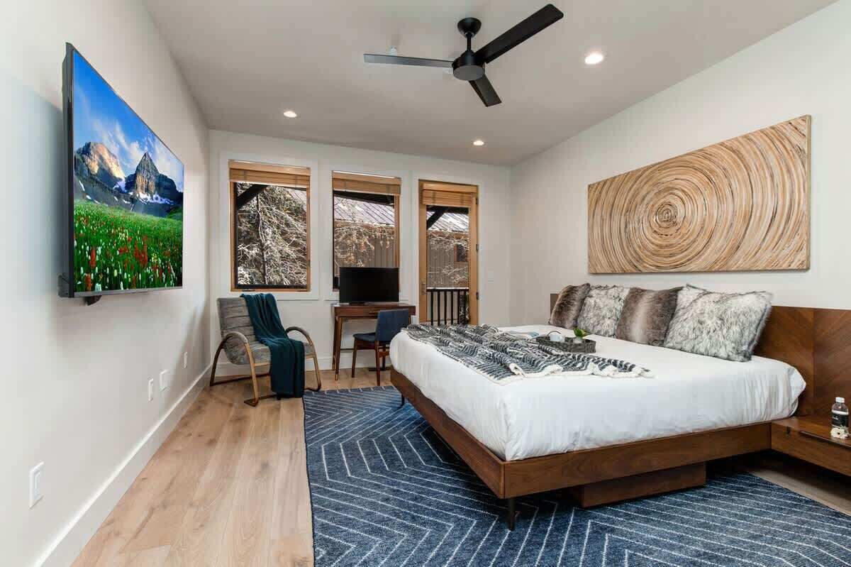 A bedroom with a bed, a desk, a chair, a TV, and a ceiling fan.
