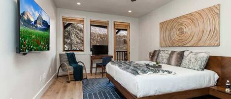 A bedroom with a bed, a desk, a chair, a TV, and a ceiling fan.
