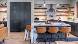 Une cuisine moderne avec des meubles de couleur sombre, un îlot central doté de tabourets de bar, un éclairage suspendu et des étagères intégrées.