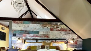 A bedroom with a large bed, a rustic wooden ceiling, a colorful wall, and a dreamcatcher hanging from the ceiling. - Funky Upstairs apartment - steps from local popular restaurant. (Arundel)