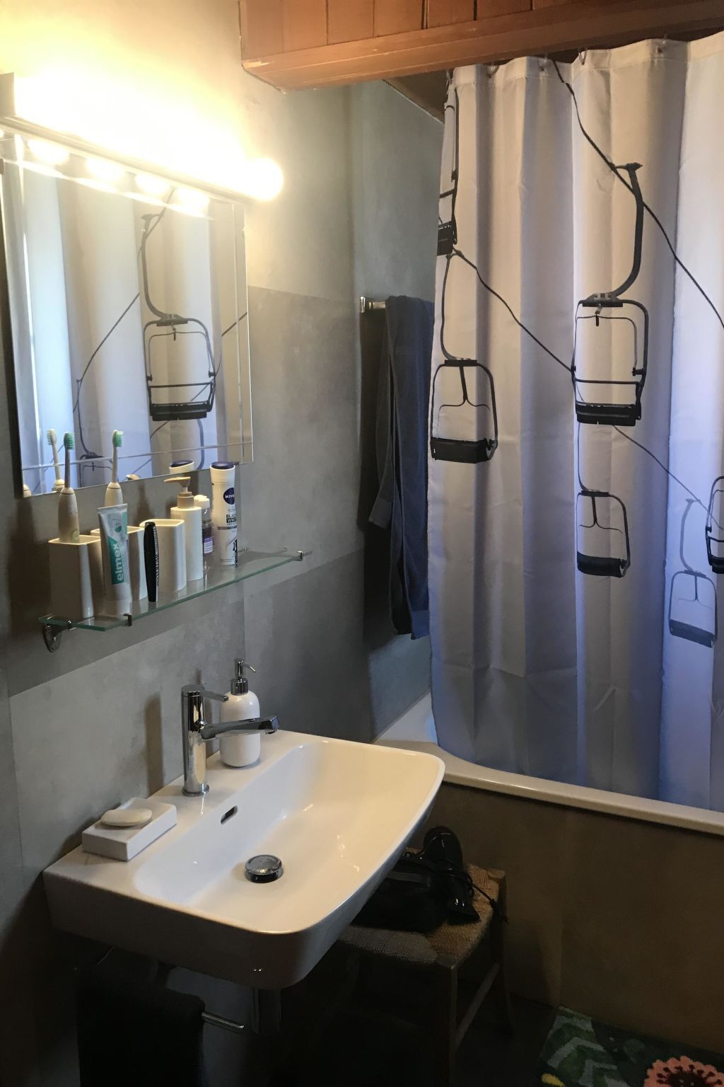 Une salle de bain avec un lavabo blanc, un miroir et un rideau de douche orné d’un motif représentant un télésiège.