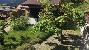 Een huis met schuin dak, omgeven door weelderige begroeiing en een berg op de achtergrond.