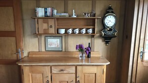 Een houten kast met meerdere lades en planken, een ingelijst foto, een vaas met bloemen, en een wandklok.