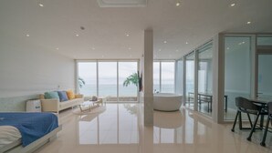A modern hotel room with a large window, a bed, a sofa, a coffee table, and a bathtub. - Daytona Pool Villa (Pohang)