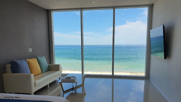 A bedroom with a large window overlooking a beach, a bed, a sofa, and a flat-screen TV. - Daytona Pool Villa (Pohang)