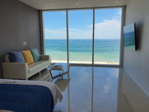 A bedroom with a large window overlooking a beach, a bed, a sofa, and a flat-screen TV. - Daytona Pool Villa (Pohang)