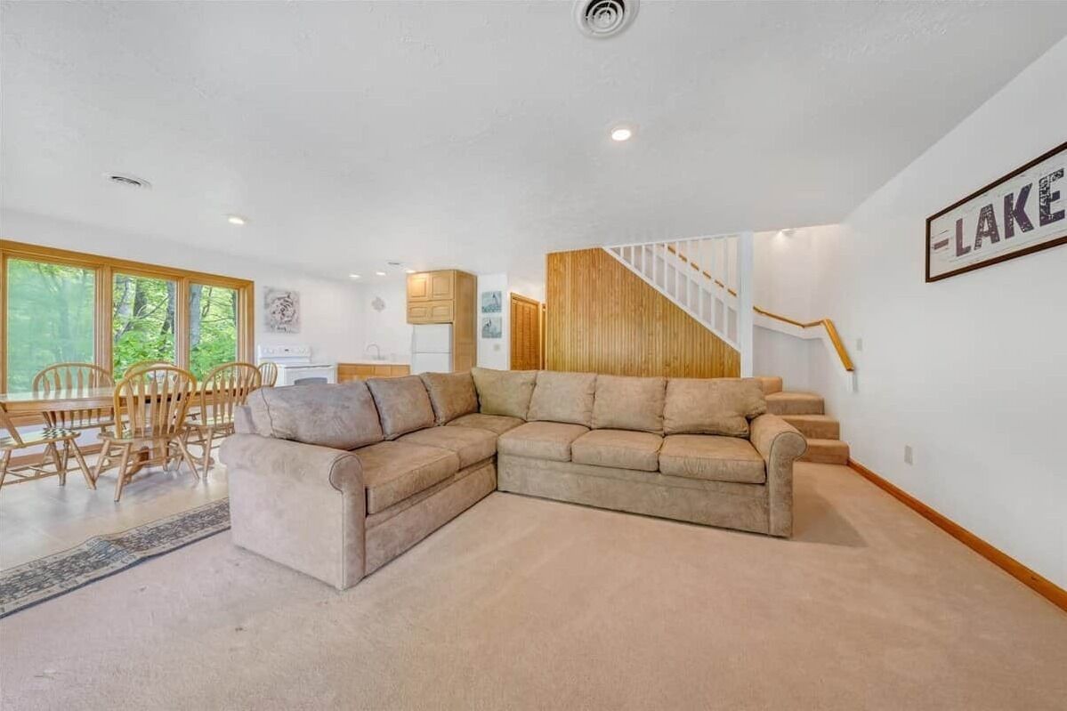Uma sala de estar moderna com um sofá seccional, uma área de jantar com cadeiras de madeira e uma escada que leva a um andar superior.
