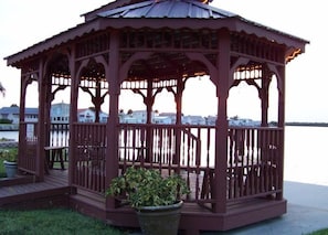 Situated on a grassy area, this classic gazebo offers a view of a body of water and surrounding residential buildings.