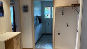 Un couloir étroit au plancher en bois mène à une cuisine avec des meubles blancs et une fenêtre.
