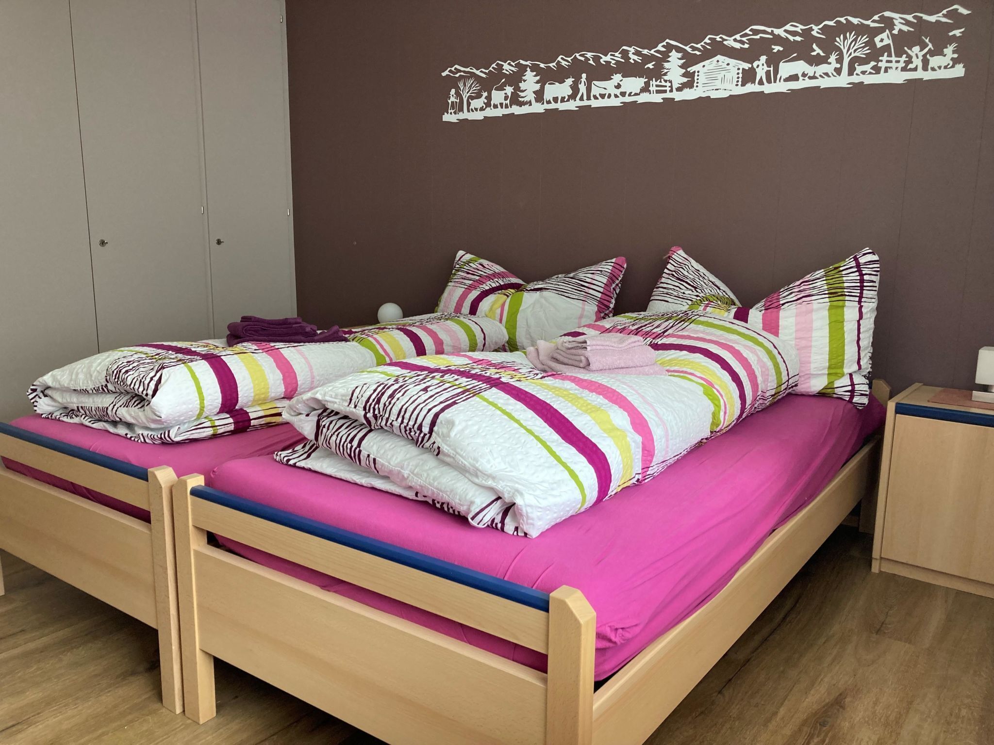 Una cama doble con ropa de cama y almohadas de colores, un cabecero de madera y un mural en la pared.