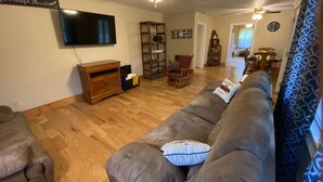 Een woonkamer met een grijze bank, een houten tv-meubel en een plafondventilator.