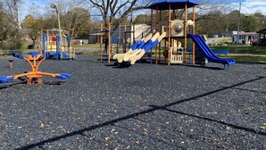Een speeltuin met diverse speeltoestellen, waaronder glijbanen en schommels, gelegen op een grindpad.