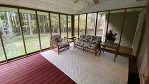 Een overdekt terras met een plafondventilator, twee rieten stoelen, een bank en een kleine tafel.