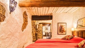 A cozy bedroom with a stone wall, a wooden ceiling, and a bed with red bedding. - Vacation home La Roq by Interhome (Roquebrune sur Argens)