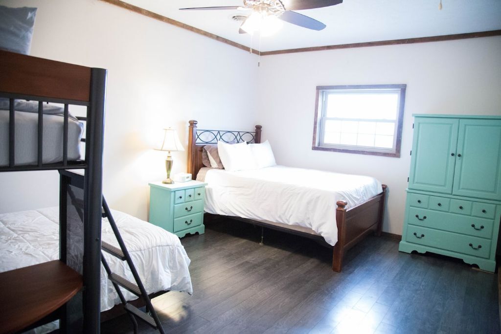 A bedroom with two beds, a window, a ceiling fan, and a green dresser.