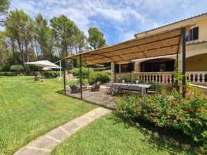 A covered outdoor seating area with tables and chairs, a stone pathway, and a garden with red flowers.