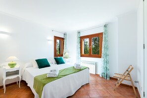 A bedroom with a bed, a nightstand, a chair, a window, and a radiator.