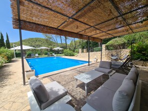 A covered outdoor swimming pool area with lounge chairs and umbrellas.