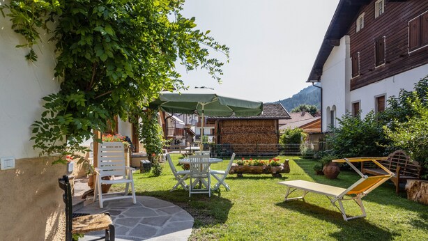 A courtyard with a stone bench, white chairs, a table, and a lounge chair.
