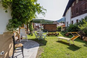 Un patio con un banco de piedra, sillas blancas, una mesa y una tumbona.