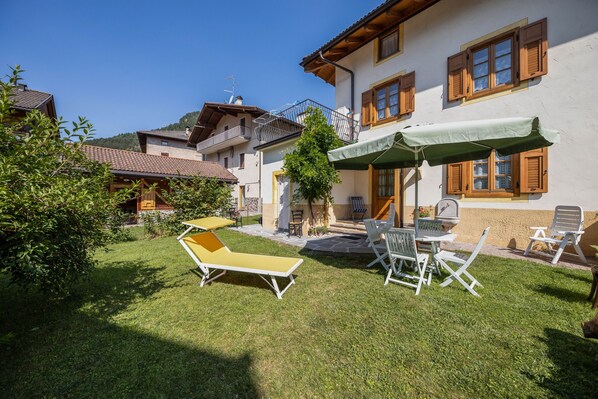 Un patio con césped, mobiliario exterior y un edificio con contraventanas de madera.