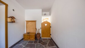 A hallway with a stone floor, wooden cabinets, a wooden door with a heart-shaped cutout, and a small shelf with a decorative item.