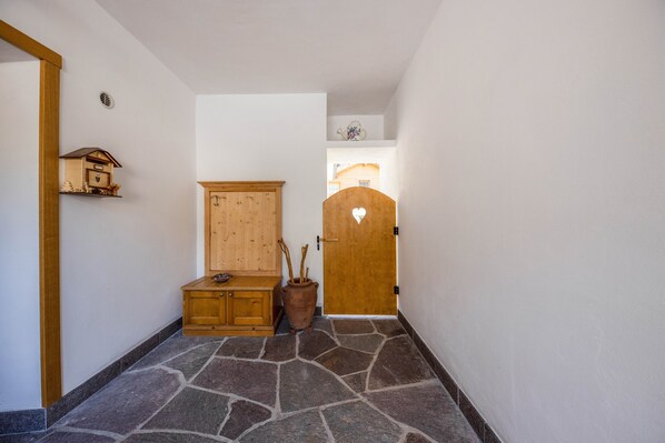 Un pasillo con suelo de piedra, armarios de madera, una puerta de madera con un recorte en forma de corazón y un estante pequeño con un adorno.