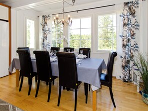 A dining room with a table set for six, surrounded by six chairs, a chandelier, and large windows with curtains. - Villa adalmina by Interhome (Lieksa)
