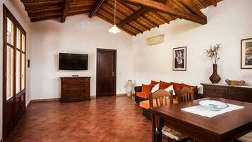 A spacious room with a wooden ceiling, a television, a sofa, a dining table, and a large window.