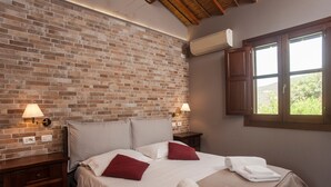 A hotel room with a brick wall, a bed with white linens, red pillows, and a window with a view. - Holiday Home "Asfodeli" with Wi-Fi, A/C & Garden (Teulada)
