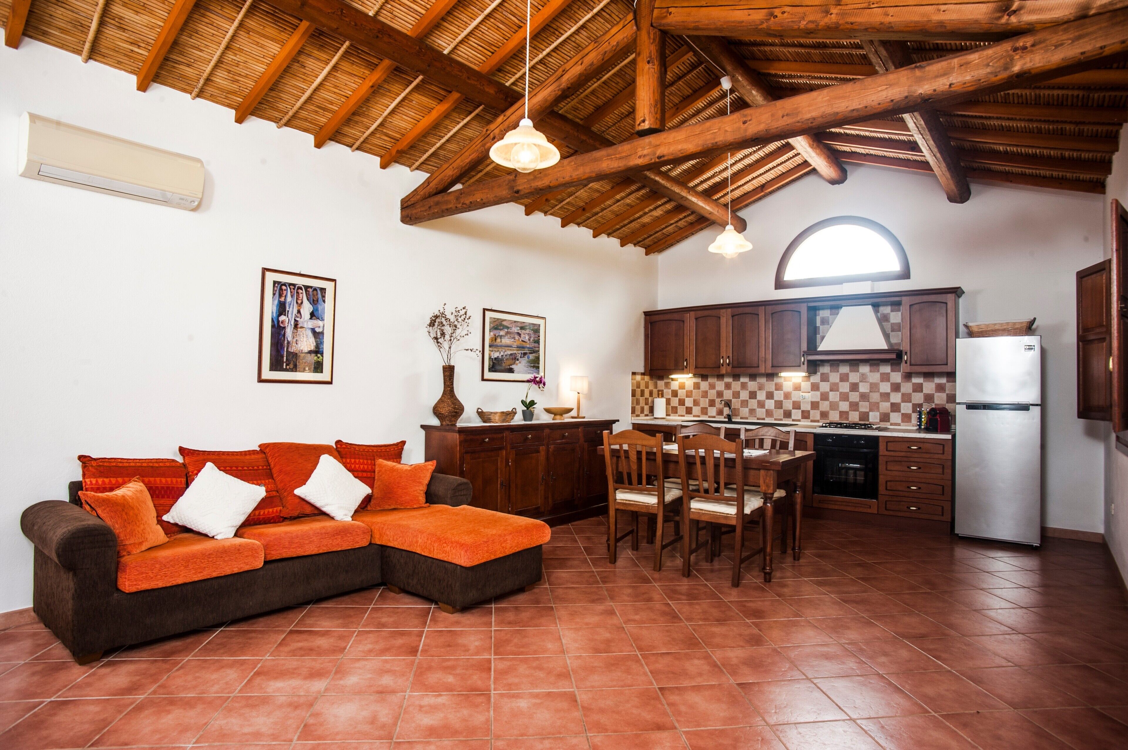 Un soggiorno con divano, tavolo da pranzo, sedie, angolo cottura con pensili ed elettrodomestici, e un alto soffitto in legno.