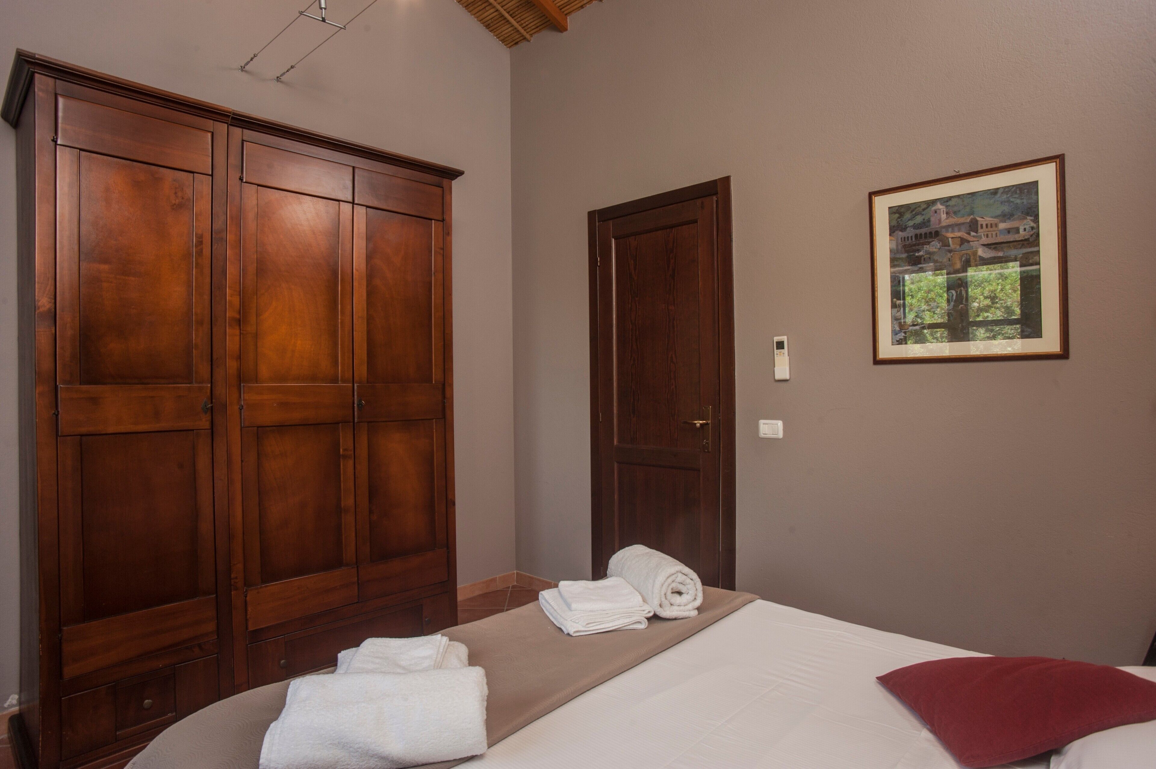 A bedroom with a bed, a wooden wardrobe, a door, and a framed picture on the wall.