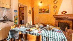 Un coin repas avec une nappe à carreaux, une cheminée et un tableau représentant des fruits accroché au mur.