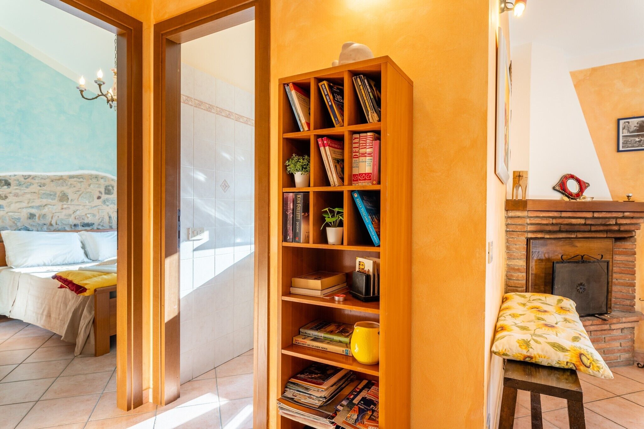 A cozy room with a bookshelf, a fireplace, a bed, and a view of a stone wall.