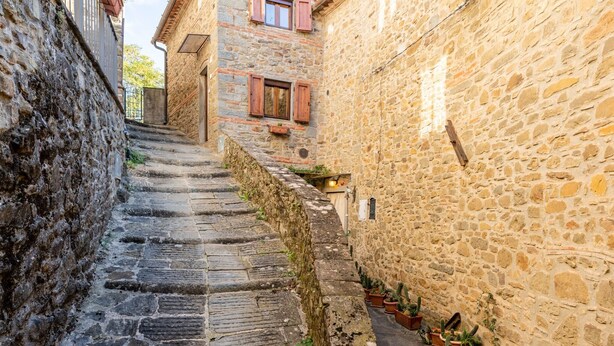 Un escalier étroit en pierre mène à un bâtiment dont le mur est également en pierre et qui est agrémenté de plantes en pot.