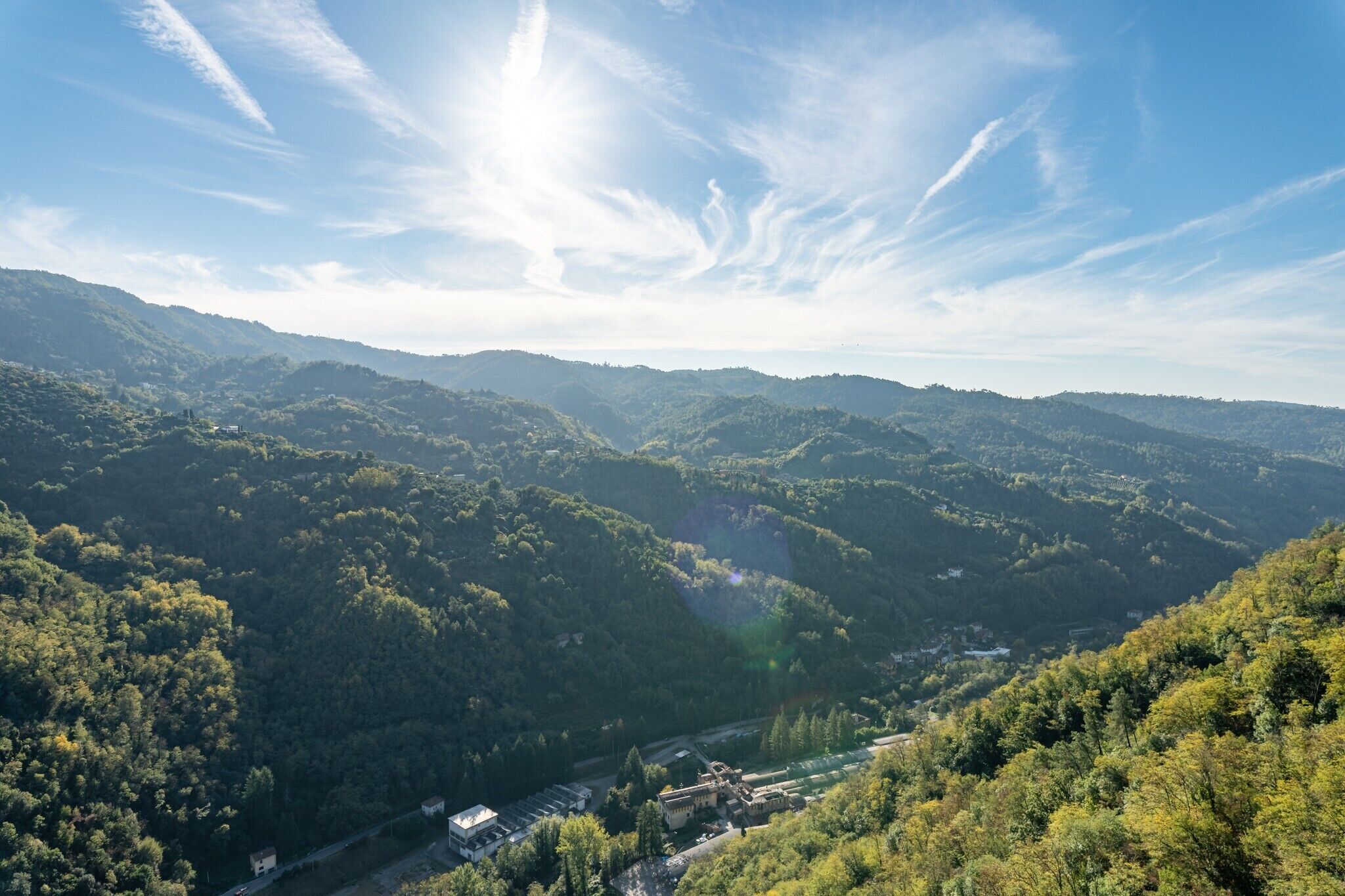 Eine gebirgige Landschaft mit einem Tal, einer Straße und Gebäuden in der Ferne.