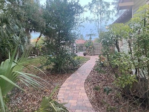 Stroll through the beautifully maintained garden pathway, lined with lush greenery and a palm tree.