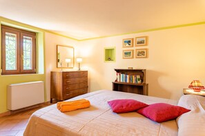 Une chambre à coucher avec un lit, une commode, un radiateur, une fenêtre et une bibliothèque.