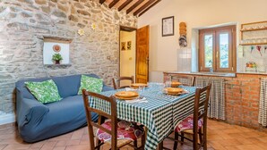 A cozy dining area with a stone wall, wooden ceiling beams, a blue sofa, and a checkered tablecloth. - Vacation Home "Il Colletto Romantic Stonehouse" with Mountain View, Garden & Terrace (Pescia)