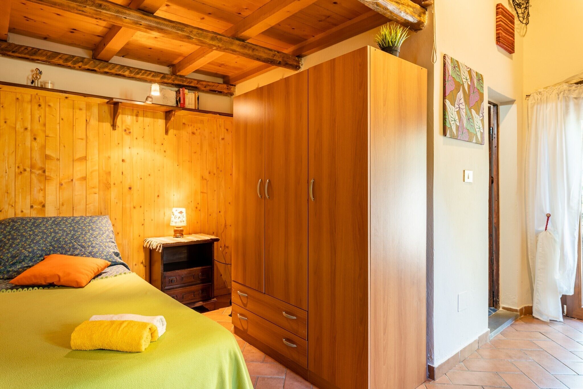 A wooden-paneled room with a bed, a wardrobe, and a small table with a lamp.